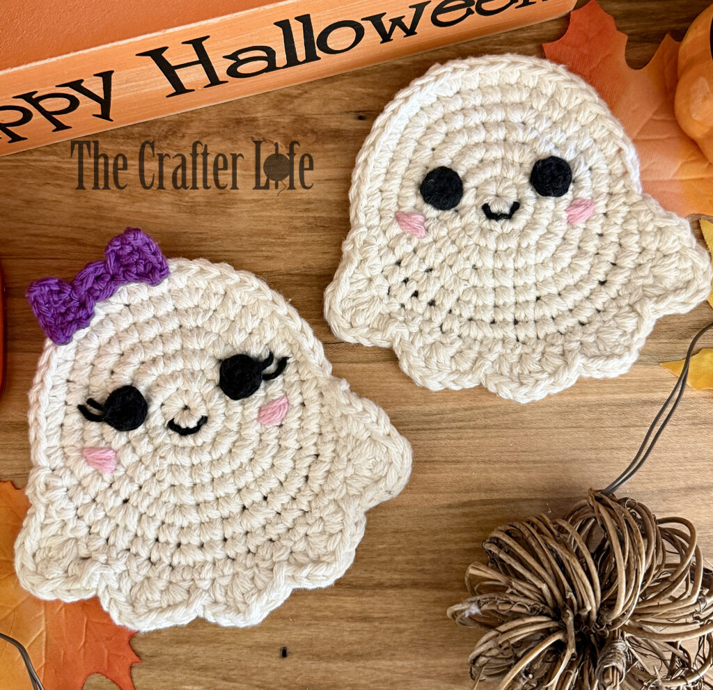 Two decorative white crochet ghost coasters laying on a wood table
